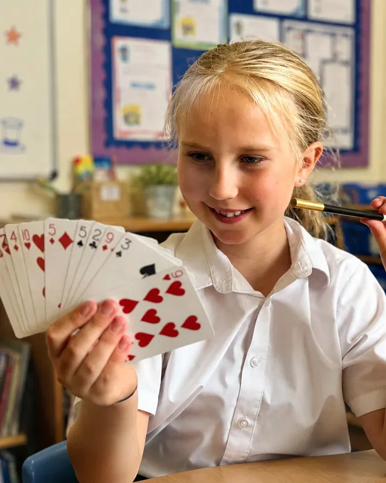 Girl performing a card trick with a fan of cards and a magic wand