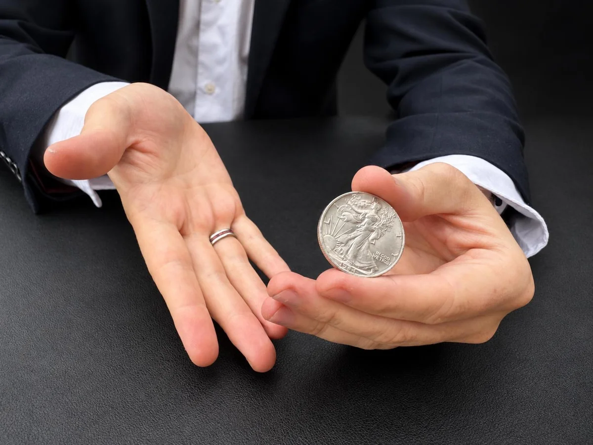 A silver half dollar coin held in a magician's hands for a coin vanish