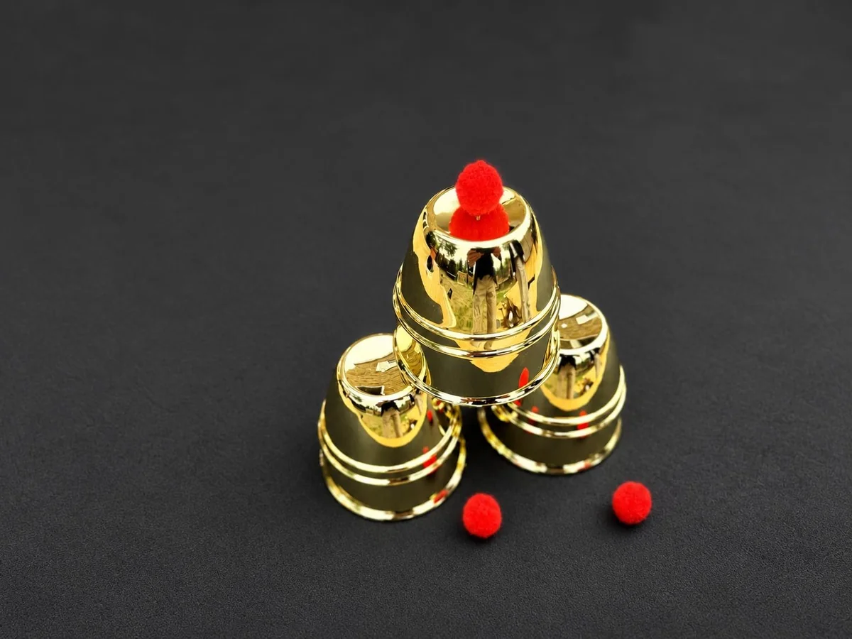 Three polished brass magic cups stacked with a red ball balanced on top